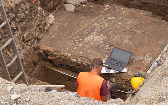 L’image montre deux archéologues au travail sur un site archéologique d’Avenches (VD). 